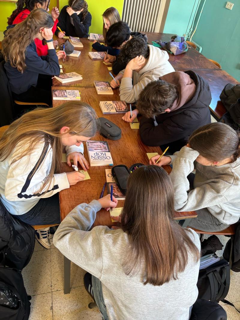 Een groep leerlingen rond de tafel met het boek 'Ossenkop', ze lezen en nemen notities