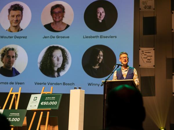 Wouter Deprez maakt de winnaars van de Boon 2024 bekend. Op de achtergrond een overzicht met foto's van de juryleden.